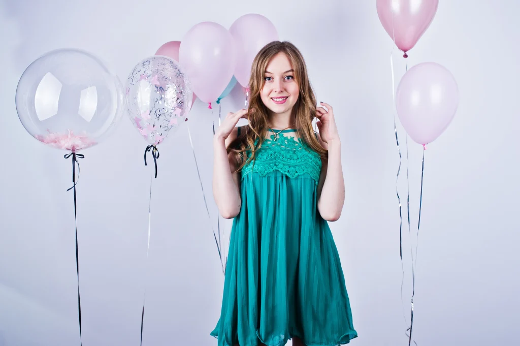 Fotografía para quince años de una joven con vestido verde agua en un estudio blanco con globos rosas detrás